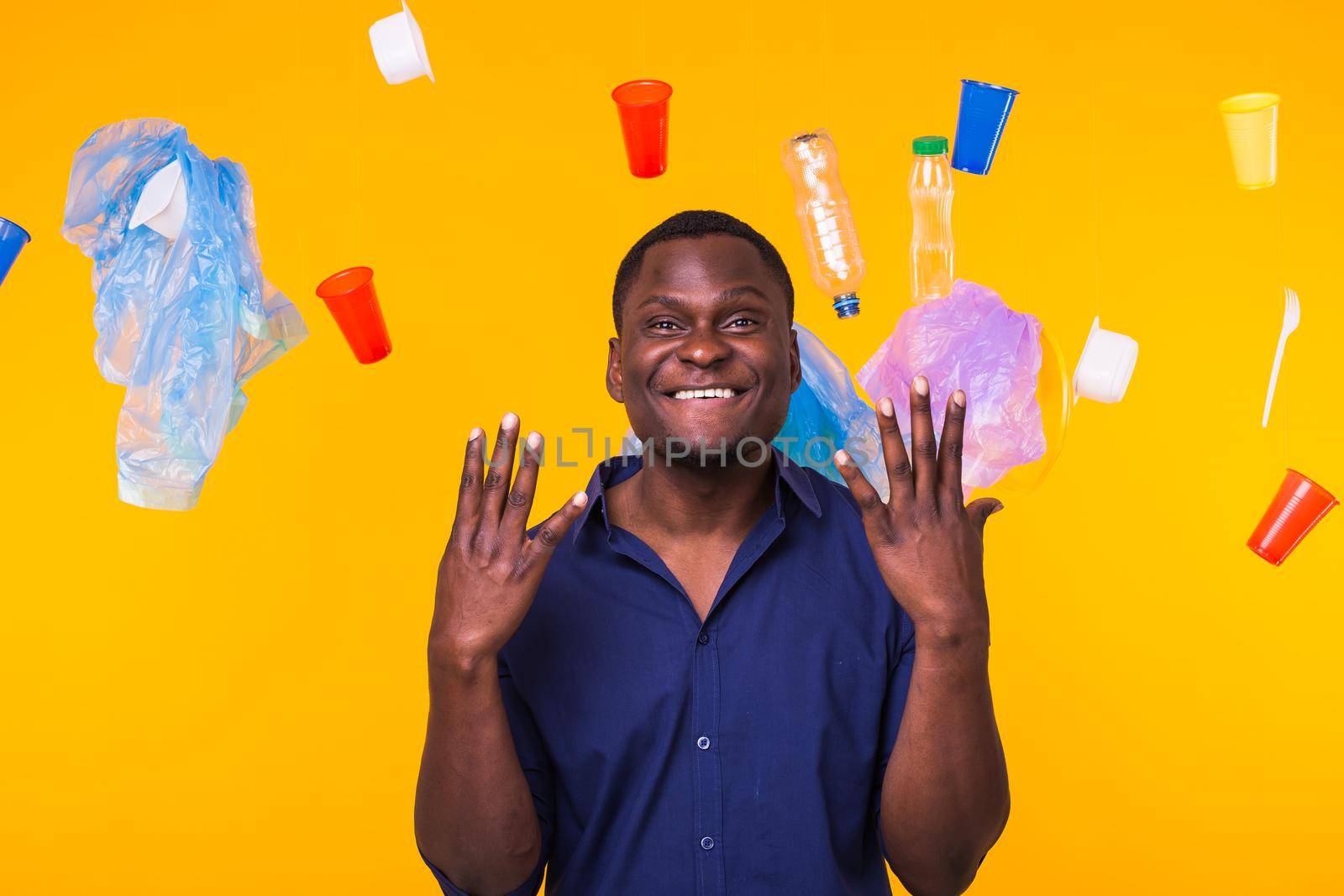 Problem of trash, plastic recycling, pollution and environmental concept - african american man is standing under trash on yellow background by Satura86