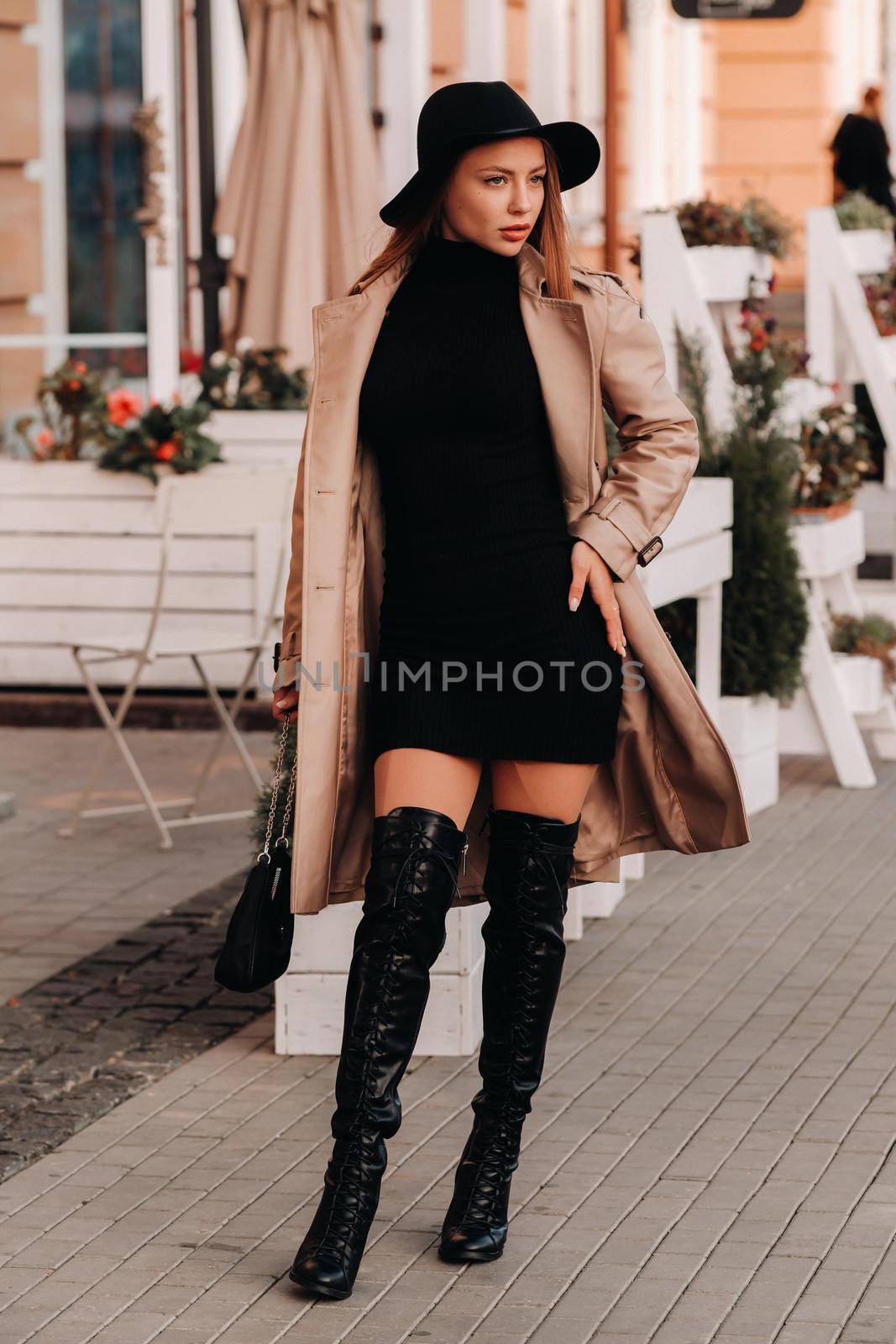 Stylish young woman in a beige coat in a black hat on a city street. Women's street fashion. Autumn clothing.Urban style.