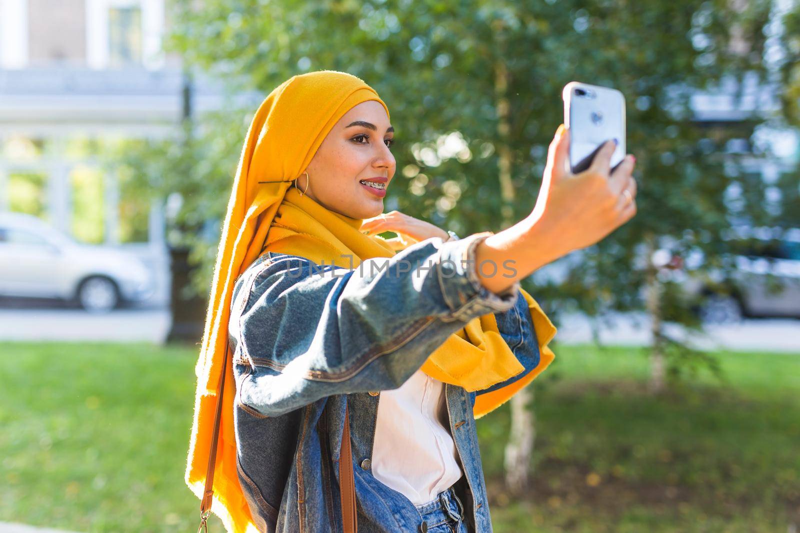Muslim girl in hijab makes a selfie on the phone standing on the street of the city.