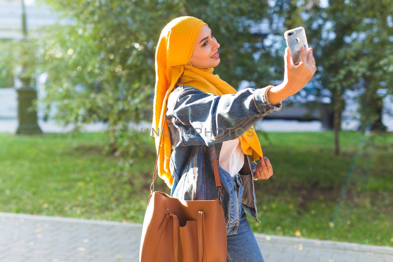 Muslim girl in hijab makes a selfie on the phone standing on the street of the city by Satura86