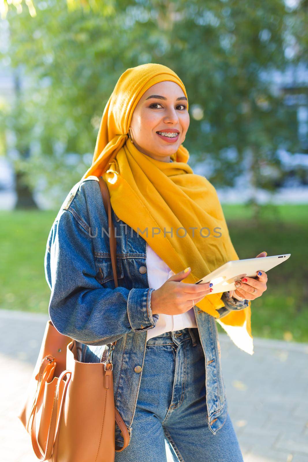 Arab woman student. Beautiful muslim female student wearing bright yellow hijab holding tablet. by Satura86