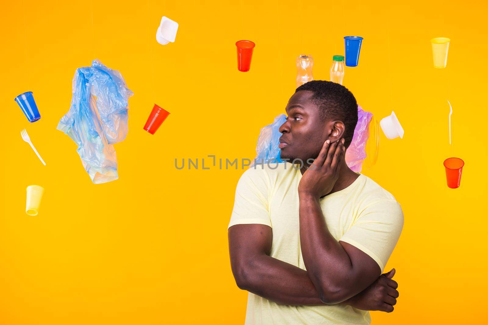 World Environment Day, plastic recycling problem and environmental disaster concept - Surprised african american man looking on trash on yellow.