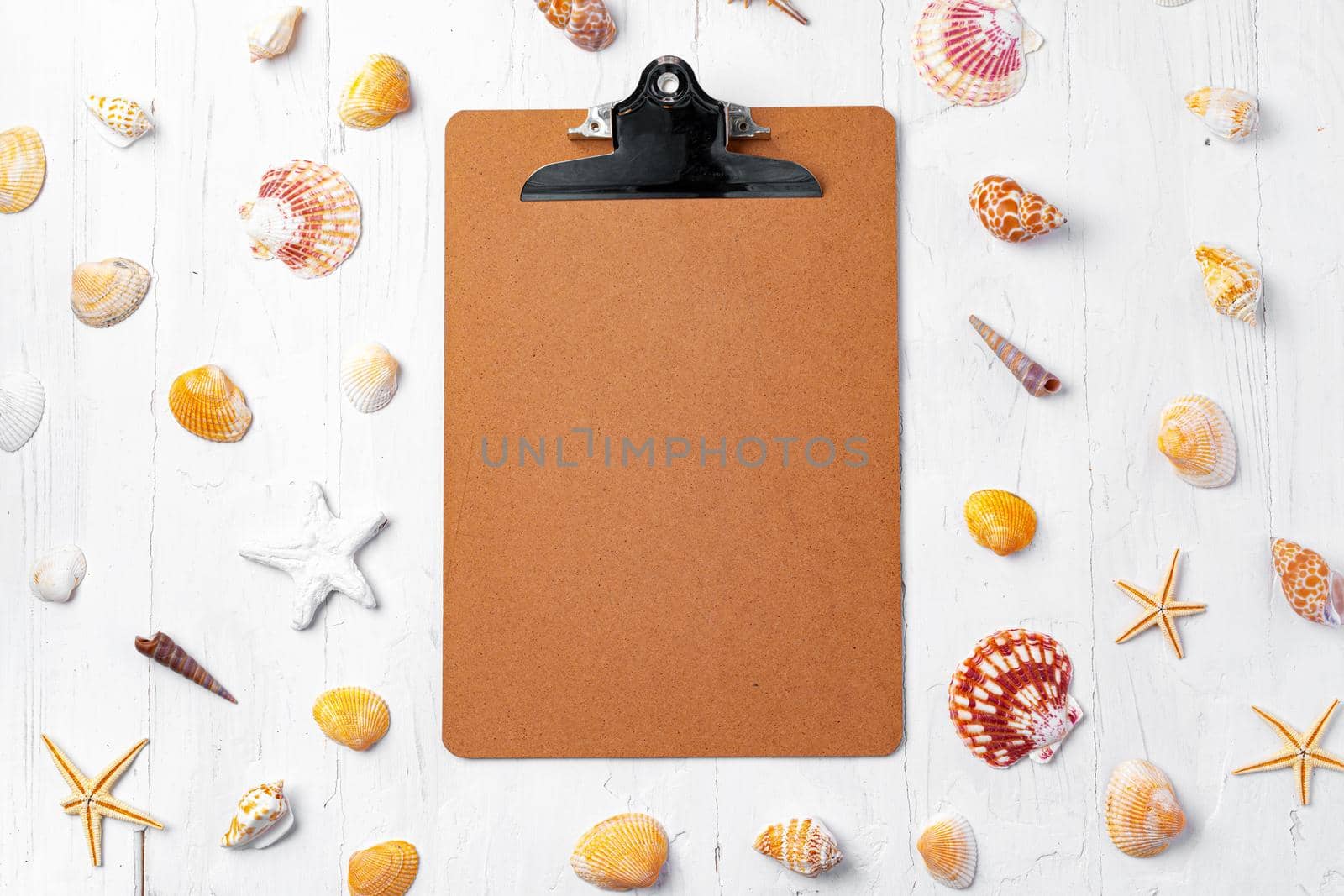 Clipboard with sea shells on white wooden table close up, copy space.