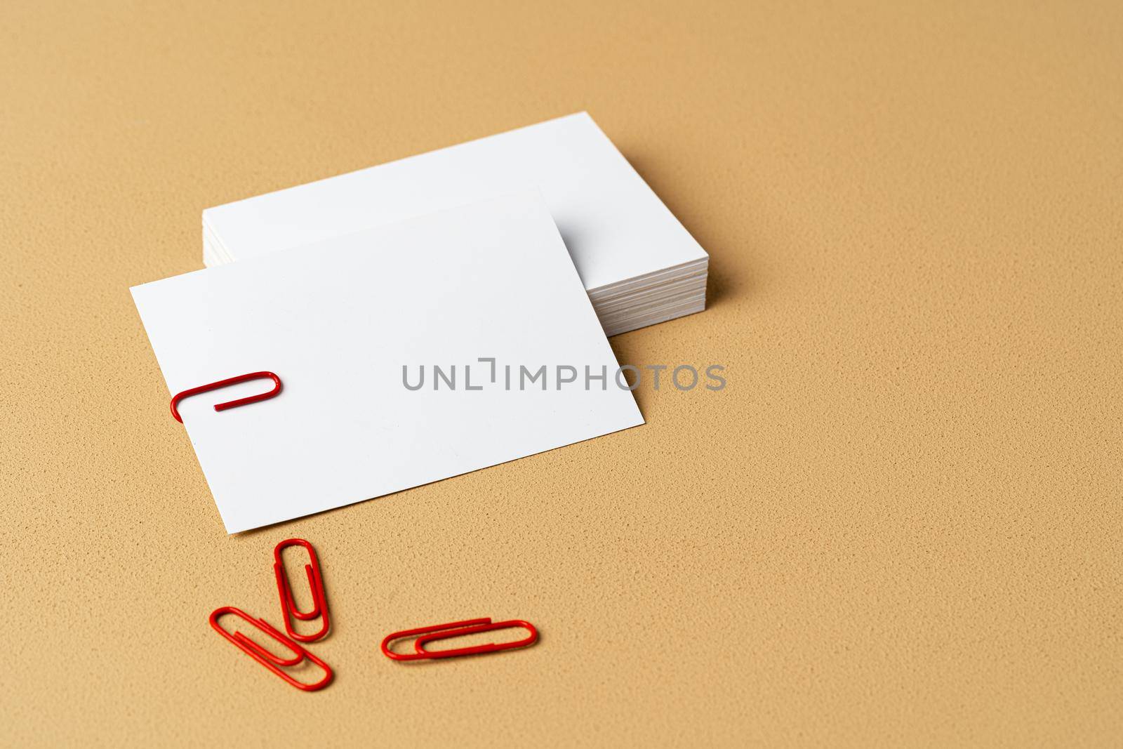 Pile of white businesscards with a clip on beige background, copy space
