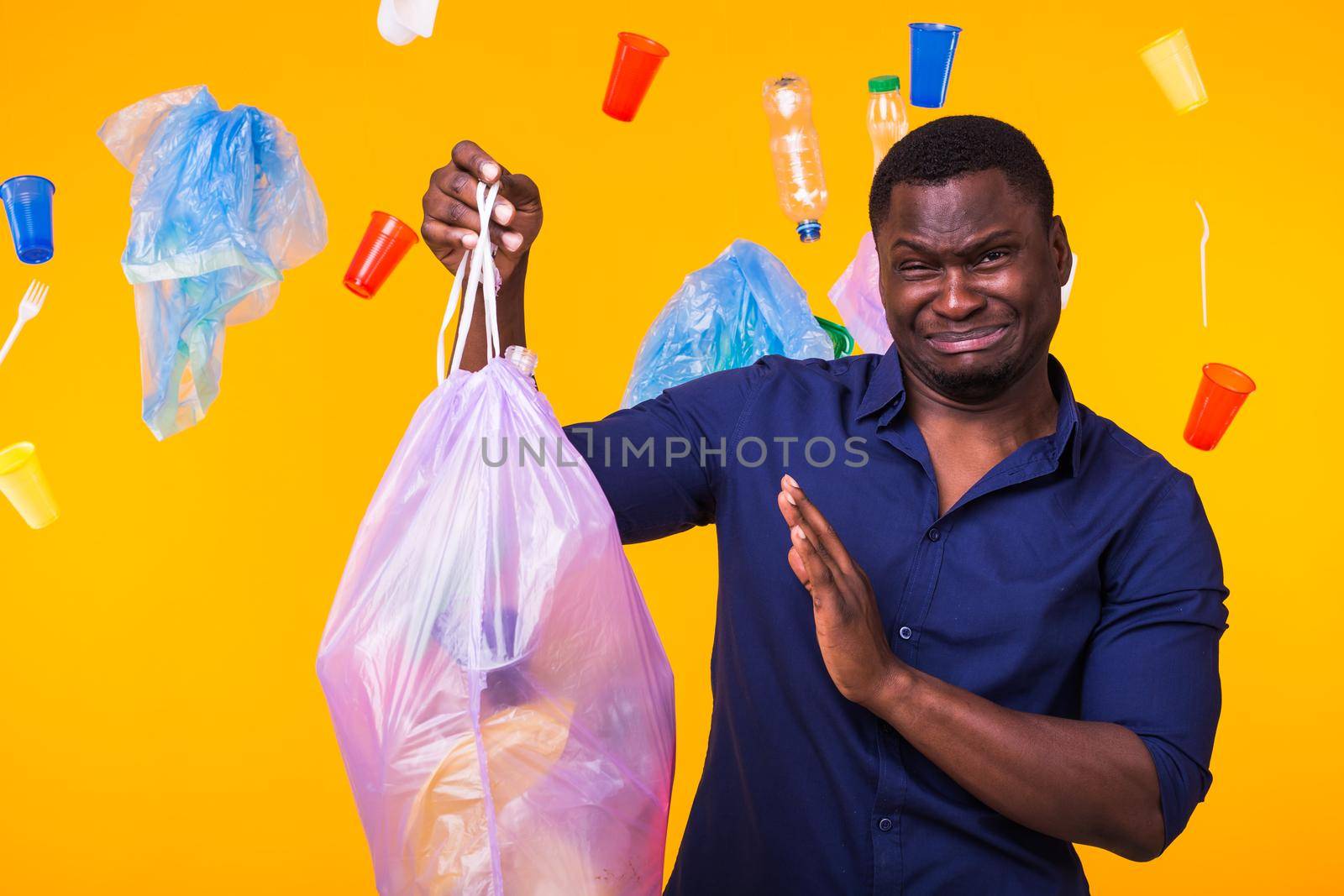 Environmental pollution, plastic recycling problem and waste disposal concept - angry man holding garbage bag on yellow background. He is feel smell of trash.