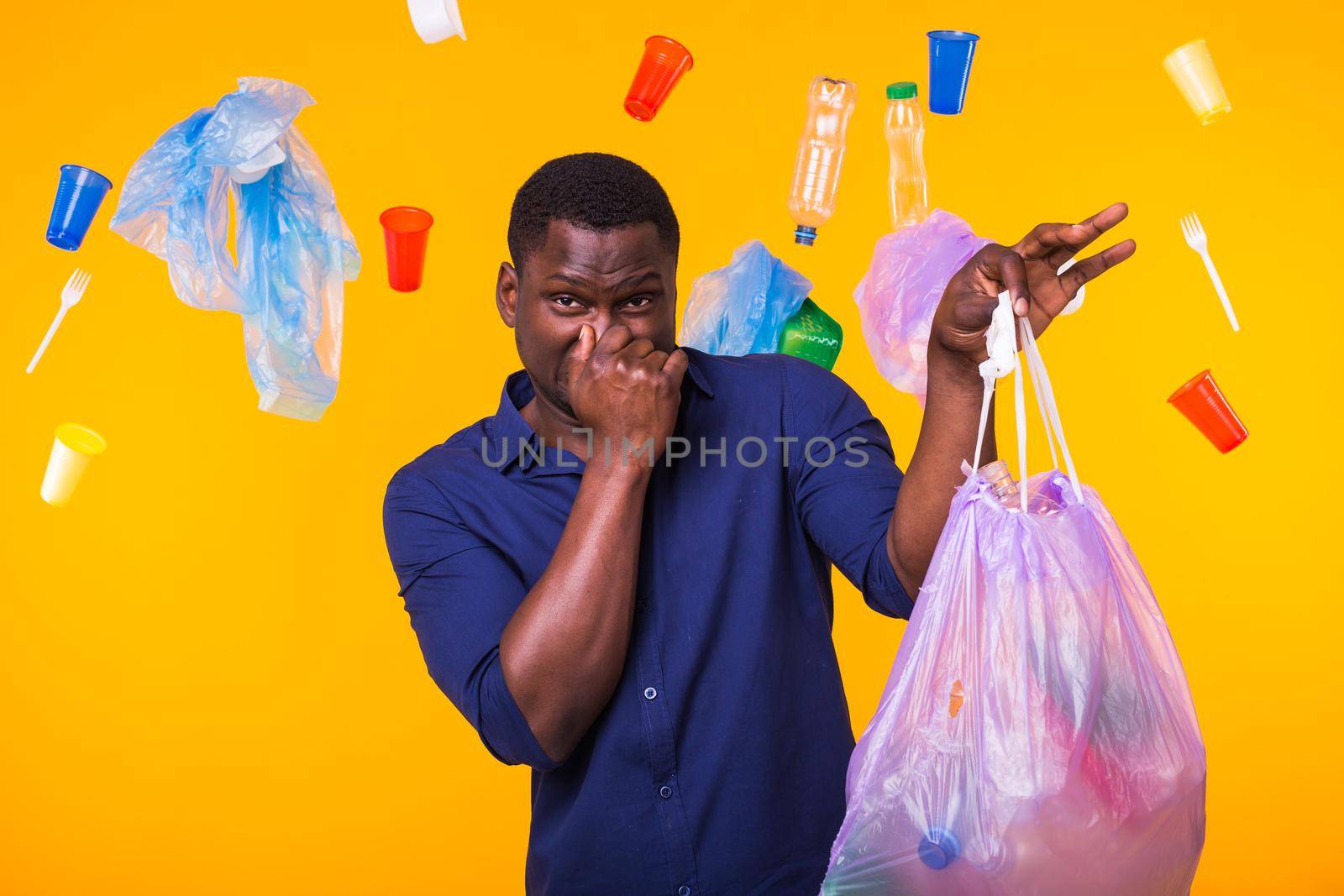 Environmental pollution, plastic recycling problem and waste disposal concept - angry man holding garbage bag on yellow background. He is feel smell of trash.