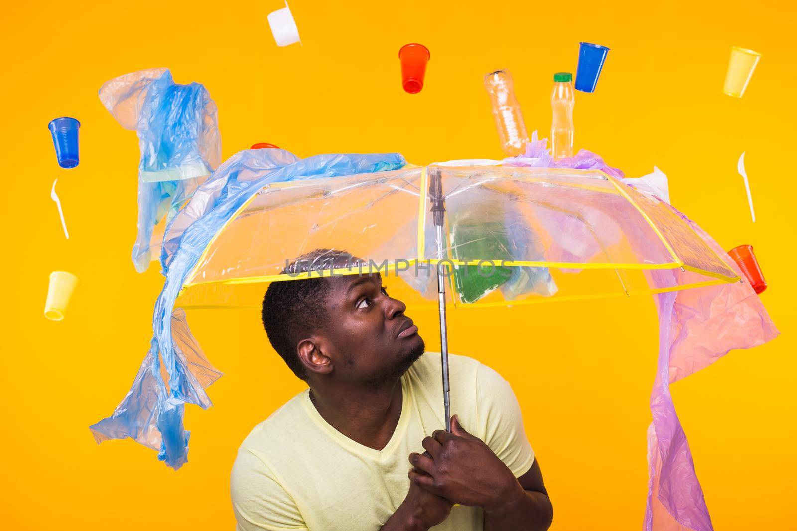 World Environment Day, plastic recycling problem and environmental disaster concept - Surprised african american man looking on trash on yellow.