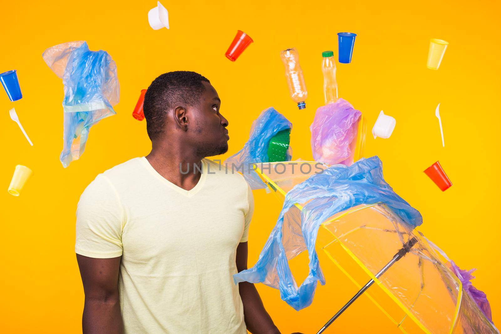 World Environment Day, plastic recycling problem and environmental disaster concept - Surprised african american man looking on trash on yellow.