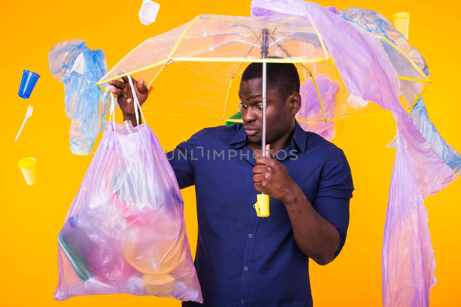 Problem of trash, plastic recycling, pollution and environmental concept - confused man carrying garbage bag on yellow background by Satura86