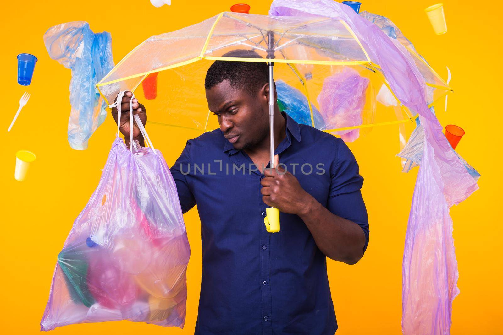 Problem of trash, plastic recycling, pollution and environmental concept - confused man carrying garbage bag on yellow background by Satura86