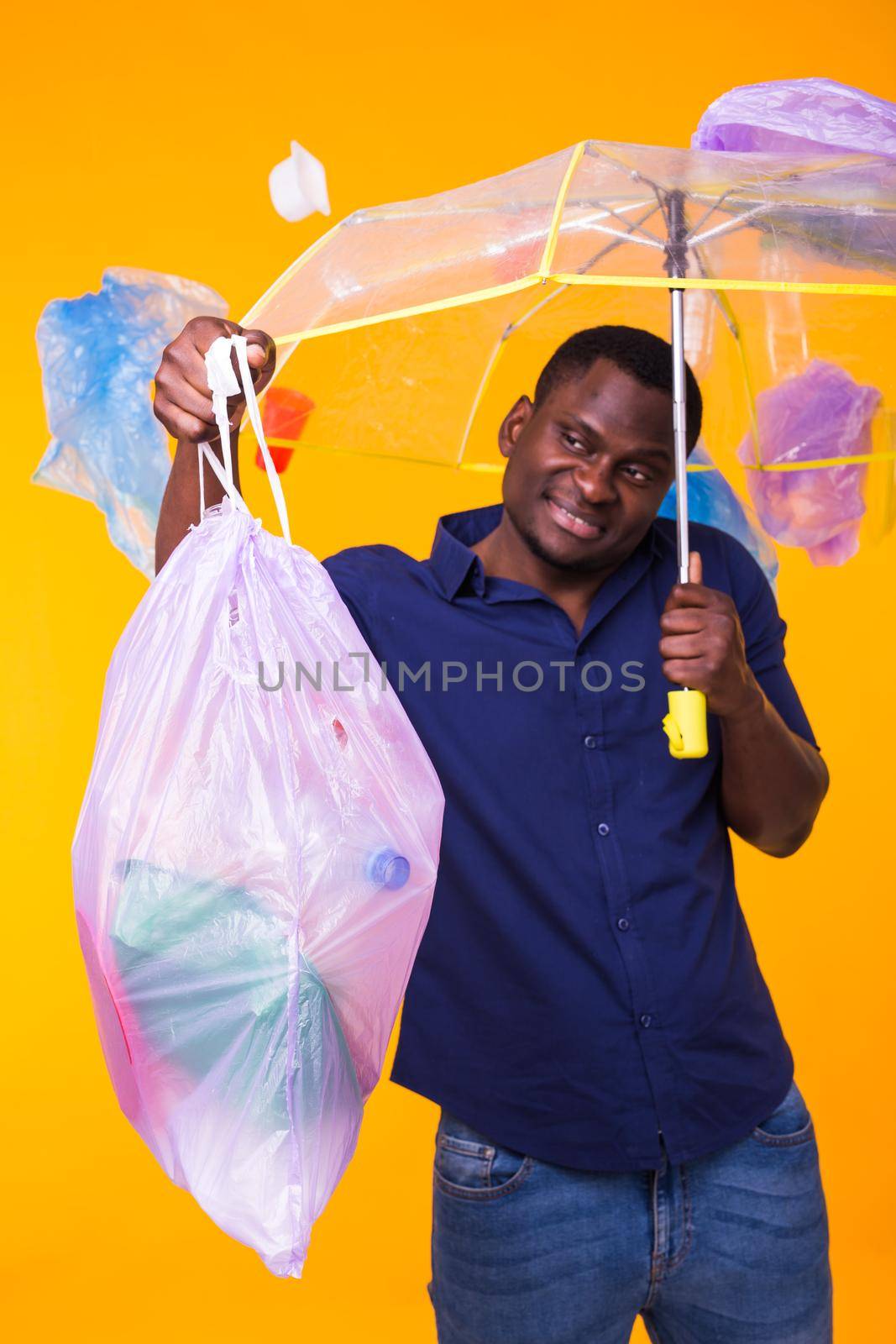 Problem of trash, plastic recycling, pollution and environmental concept - funny african american man carrying garbage for recycling on yellow background. by Satura86