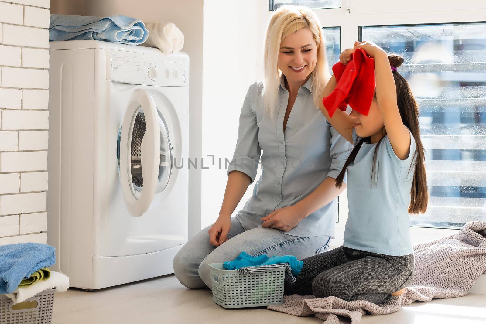 family mother and child girl little helper in laundry room near washing machine and dirty clothes by Andelov13