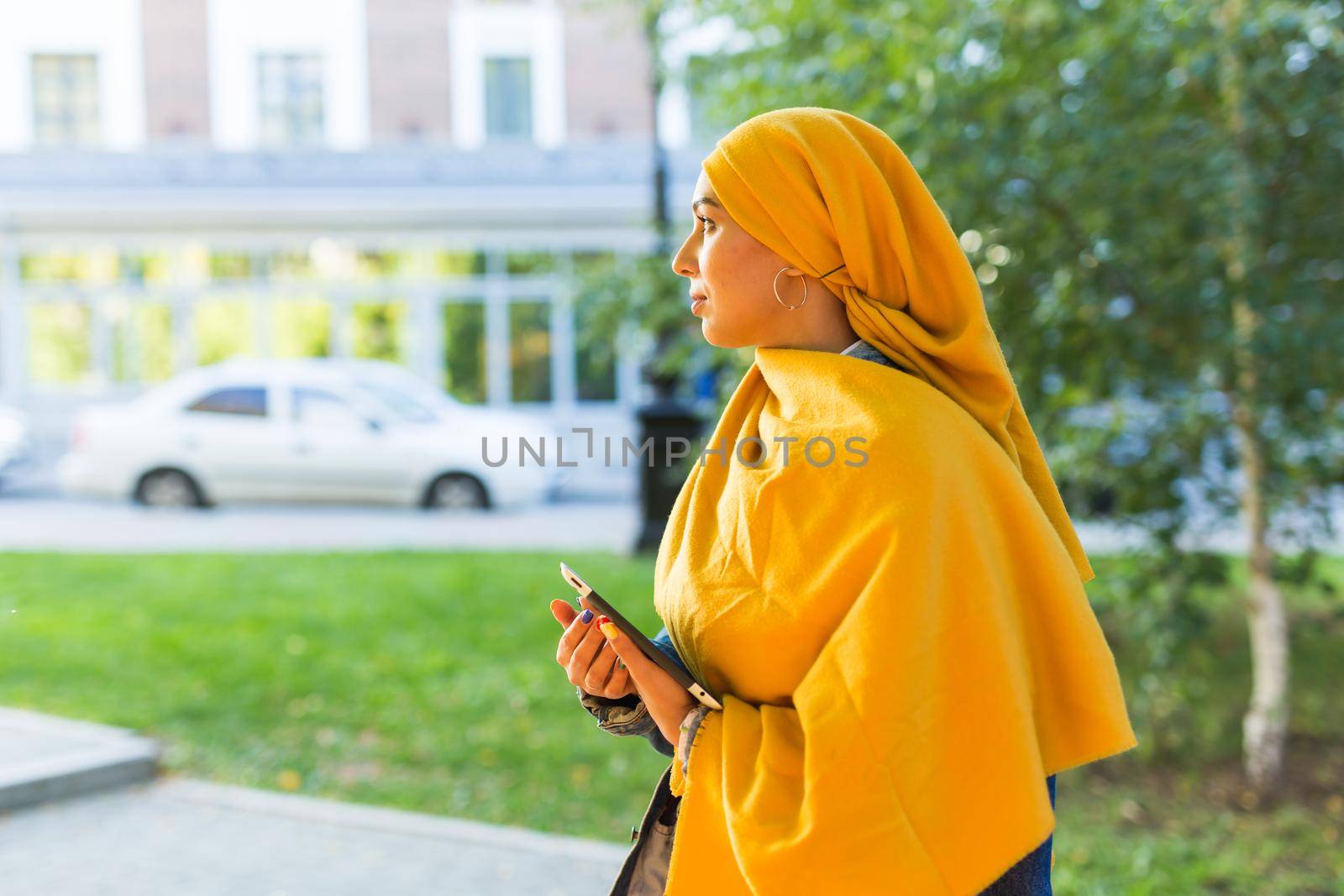 Arab woman student. Beautiful muslim female student wearing bright yellow hijab holding tablet. by Satura86