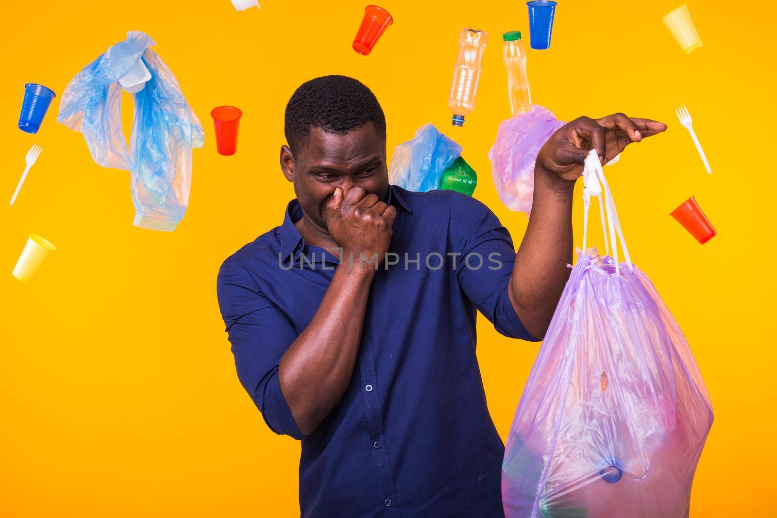 Environmental pollution, plastic recycling problem and waste disposal concept - angry man holding garbage bag on yellow background. He is feel smell of trash.