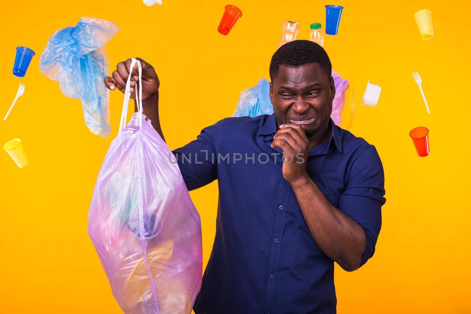 Environmental pollution, plastic recycling problem and waste disposal concept - angry african american man holding garbage bag on yellow background. He is feel smell of trash. by Satura86