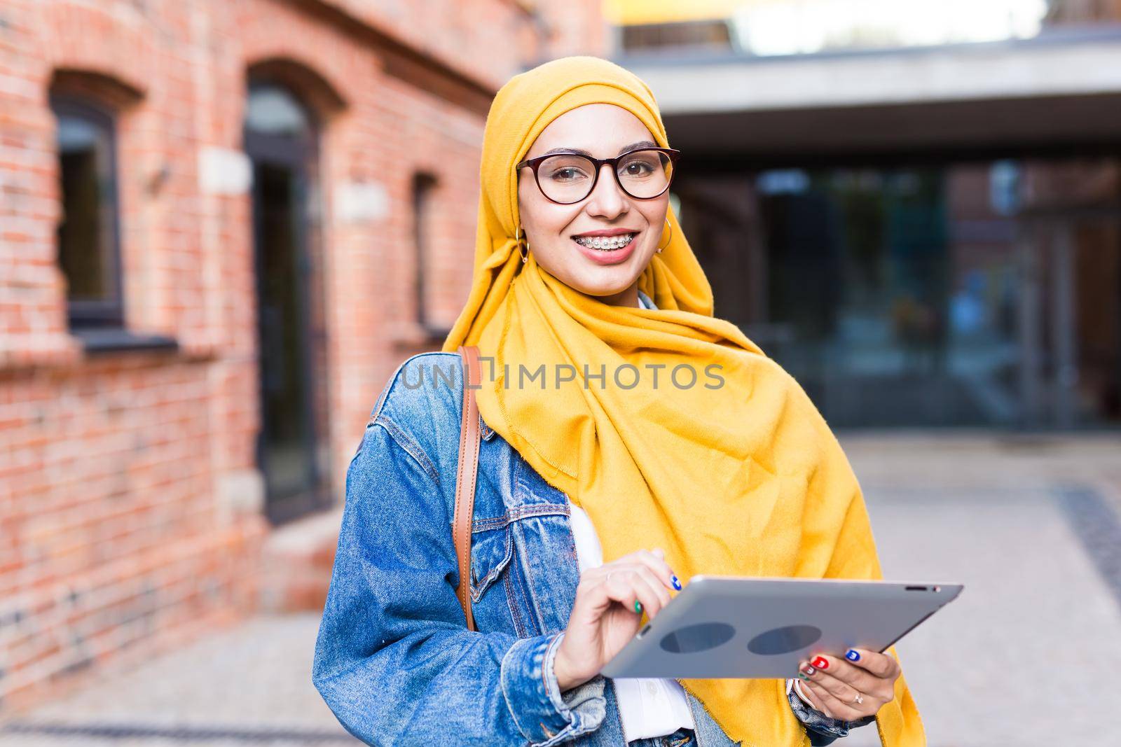 Arab woman student. Beautiful muslim female student wearing bright yellow hijab holding tablet. by Satura86