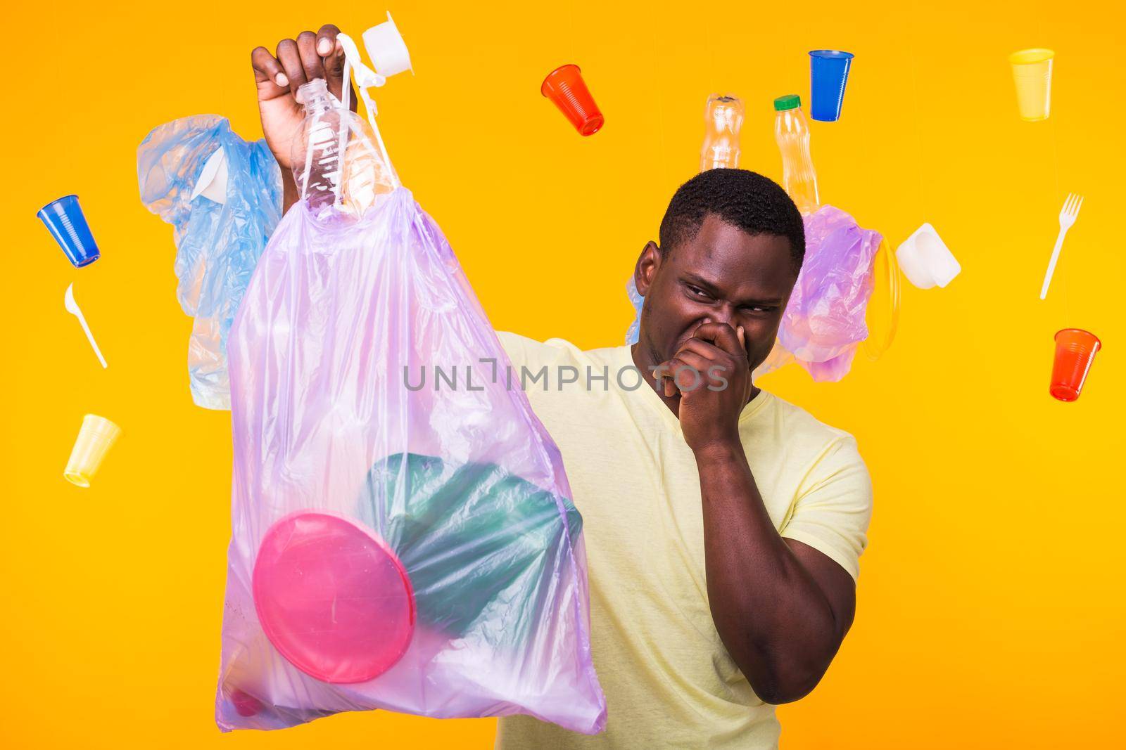 Environmental pollution, plastic recycling problem and waste disposal concept - angry african american man holding garbage bag on yellow background. He is feel smell of trash. by Satura86