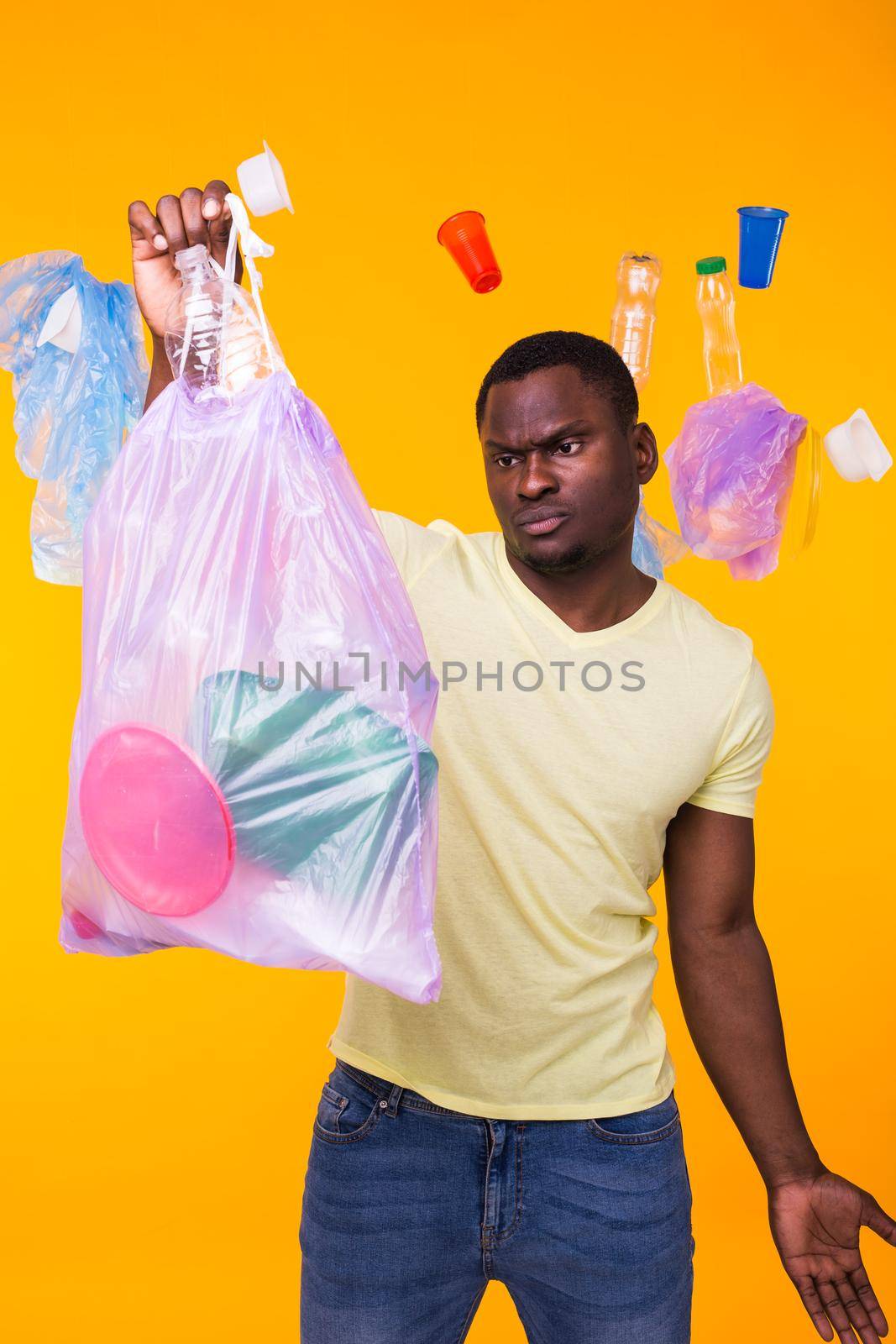 Problem of trash, plastic recycling, pollution and environmental concept - man carrying garbage bag on yellow background.