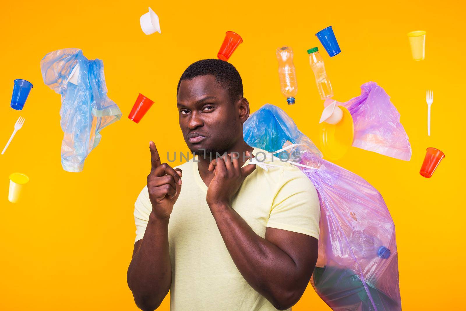 Problem of trash, plastic recycling, pollution and environmental concept - african american man carrying garbage for recycling and pointing up on yellow.