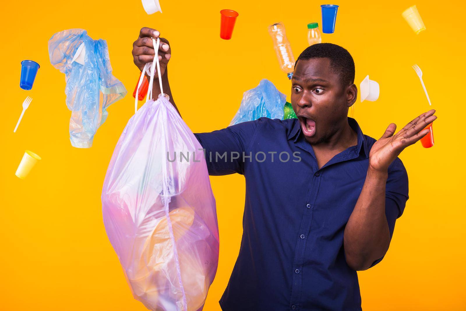 Problem of trash, plastic recycling, pollution and environmental concept - surprised man carrying garbage bag on yellow background.