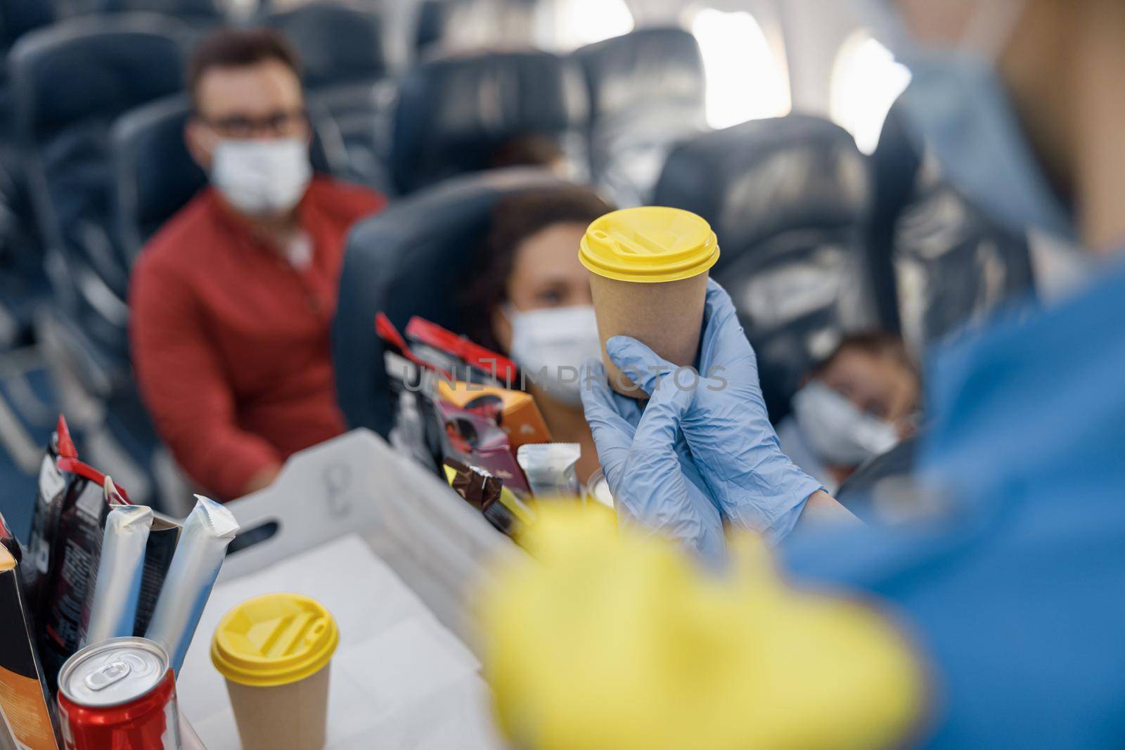 Close up shot of hands in protective gloves of flight attendant serving drinks to passengers on board. Traveling by airplane during Covid19 pandemic by Yaroslav_astakhov
