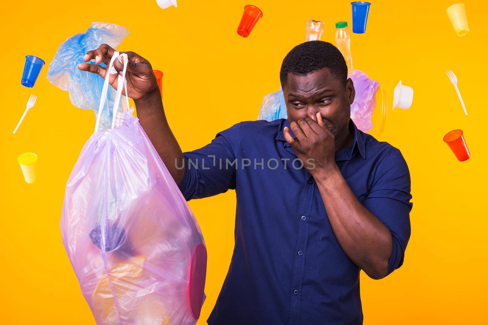 Environmental pollution, plastic recycling problem and waste disposal concept - angry man holding garbage bag on yellow background. He is feel smell of trash.