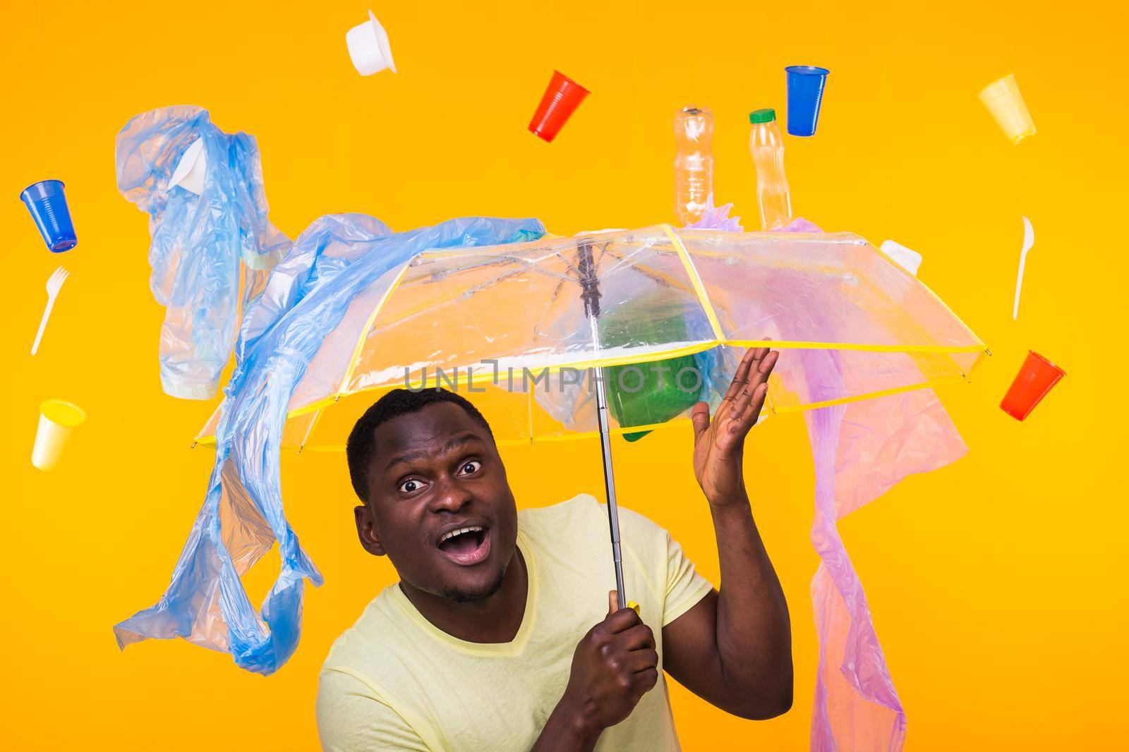 Plastic recycling problem, ecology and environmental disaster concept - Scared man screaming on yellow background with trash. He is worried about ecology disaster.