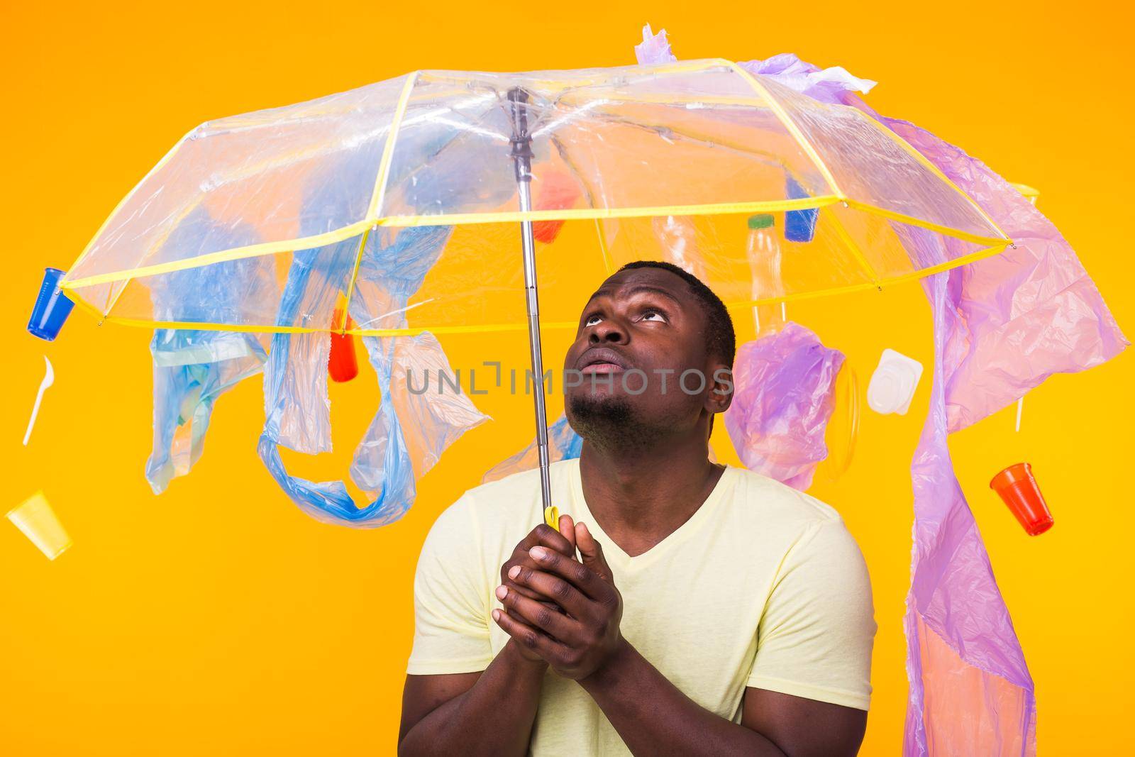 World Environment Day, plastic recycling problem and environmental disaster concept - Surprised african american man looking on trash on yellow.