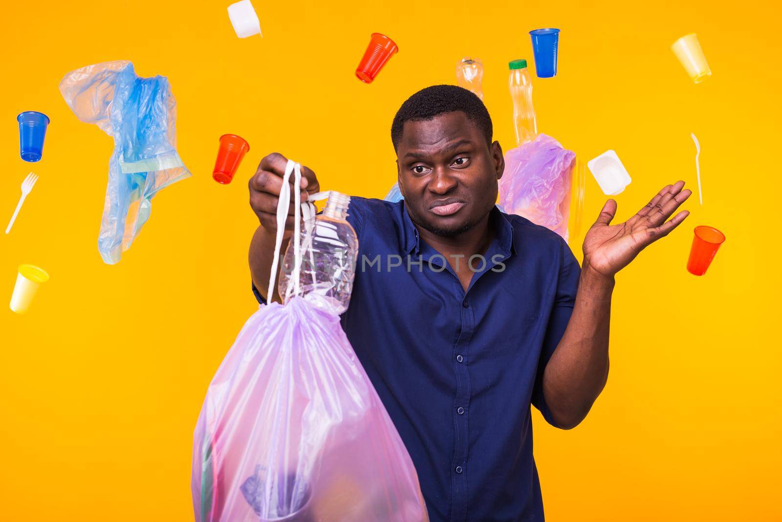 Problem of trash, plastic recycling, pollution and environmental concept - confused man carrying garbage bag on yellow background.