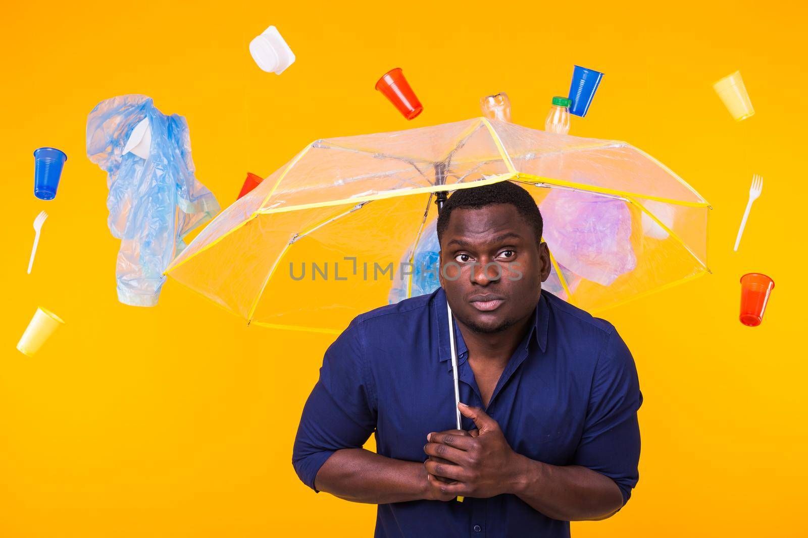 Problem of trash, plastic recycling, pollution and environmental concept - pensive african american man on yellow background with garbage