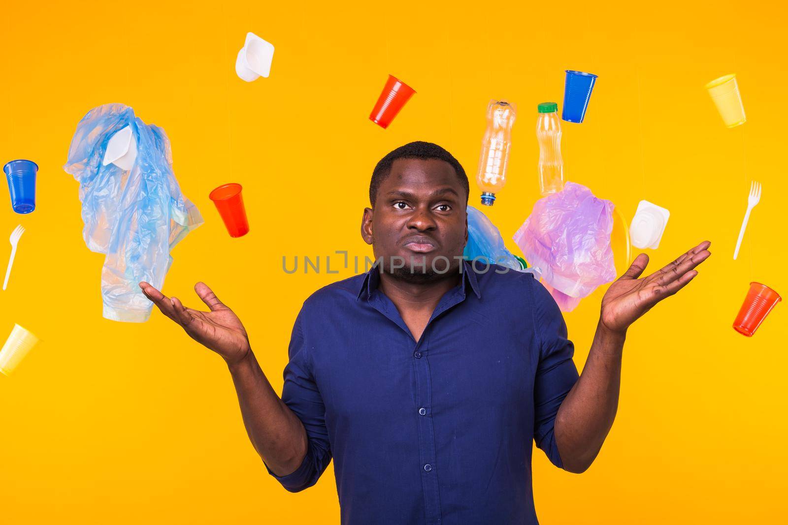 Problem of trash, plastic recycling, pollution and environmental concept - pensive african american man on yellow background with garbage