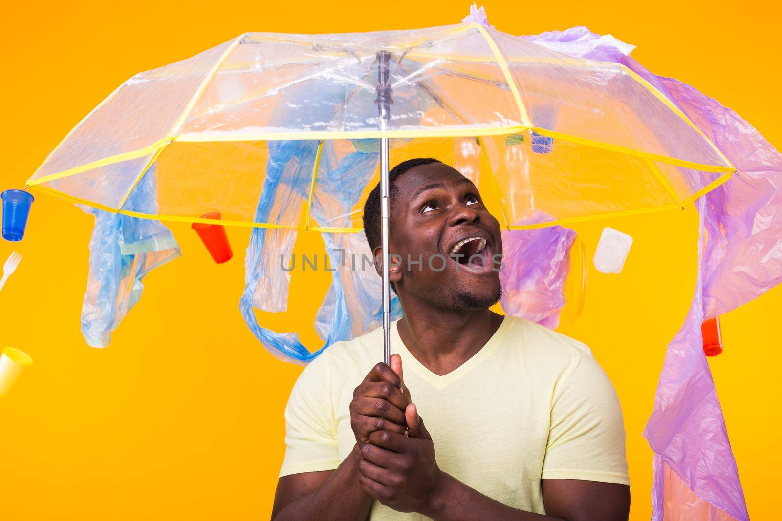 Plastic recycling problem, ecology and environmental disaster concept - Surprised african american man on yellow background with trash. He's worried about ecology disaster