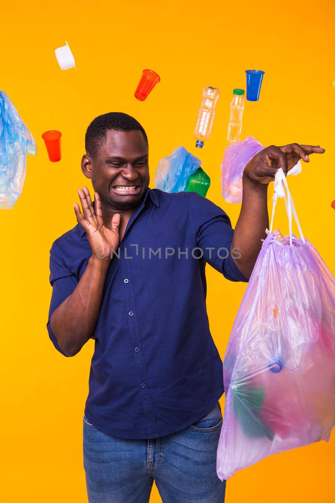 Problem of trash, plastic recycling, pollution and environmental concept - confused man carrying garbage bag on yellow background.