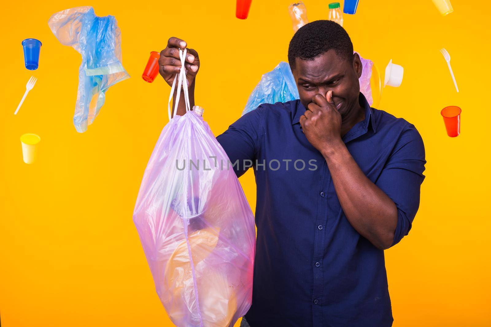 Environmental pollution, plastic recycling problem and waste disposal concept - angry man holding garbage bag on yellow background. He is feel smell of trash.