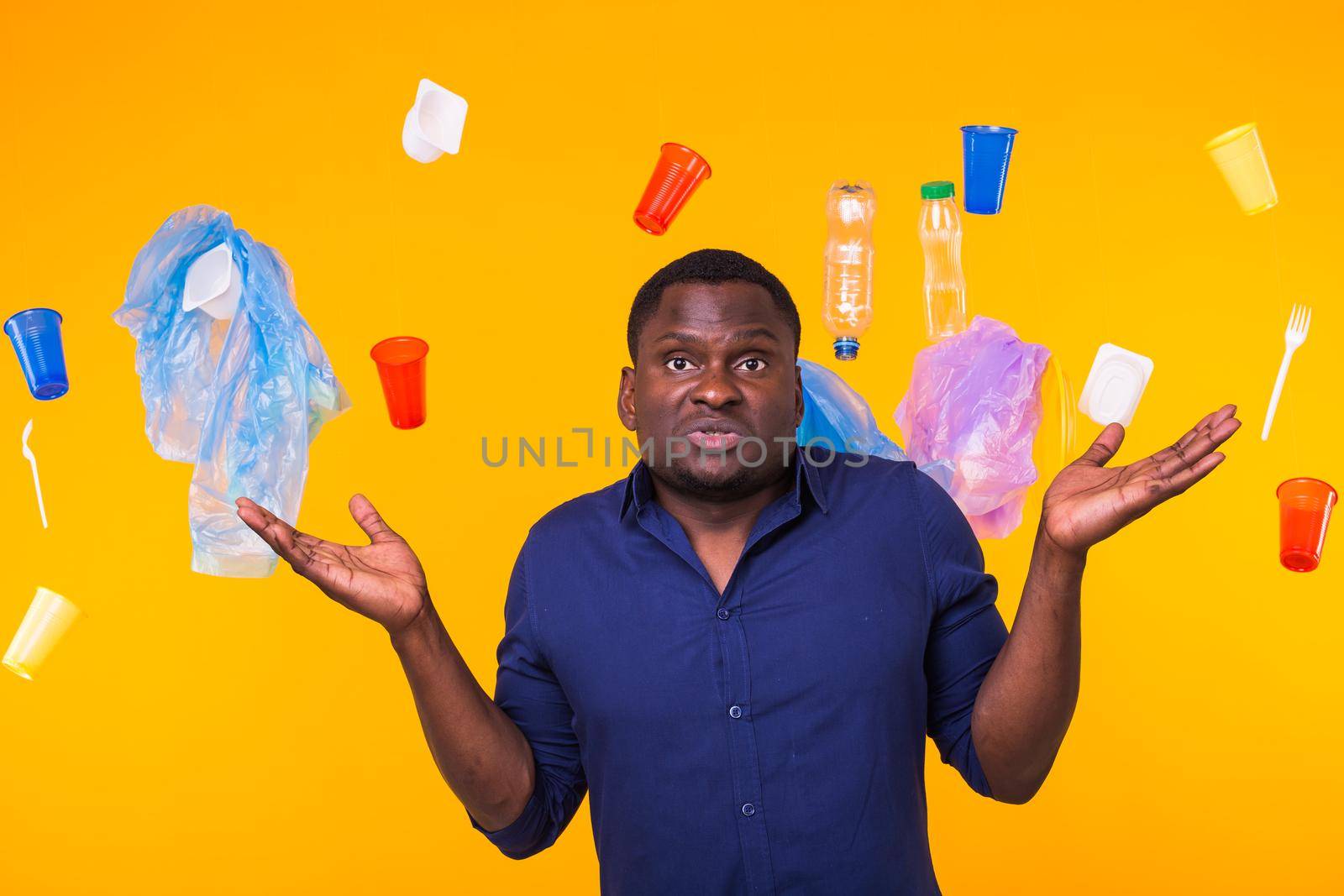 Problem of trash, plastic recycling, pollution and environmental concept - pensive african american man on yellow background with garbage