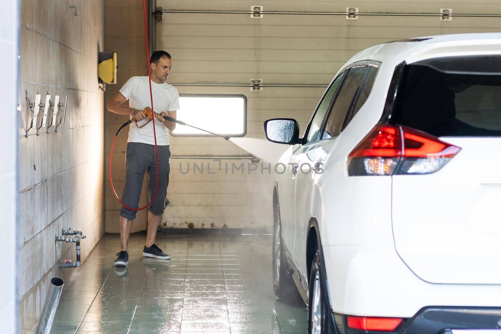 Young tall man spalshing his car by garden hose