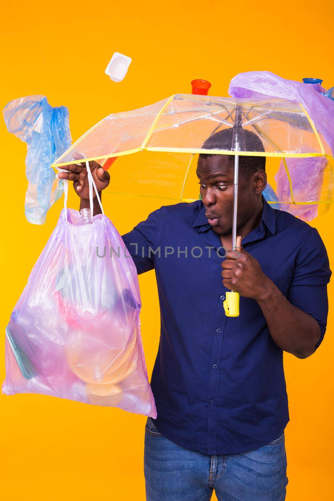 Problem of trash, plastic recycling, pollution and environmental concept - surprised african american man carrying garbage for recycling on yellow. by Satura86