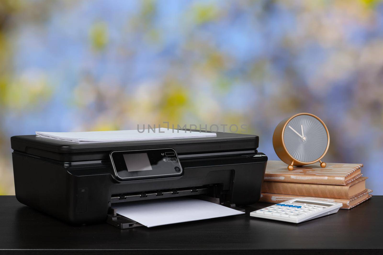 Compact home printer on desk with books against blurred background, close up