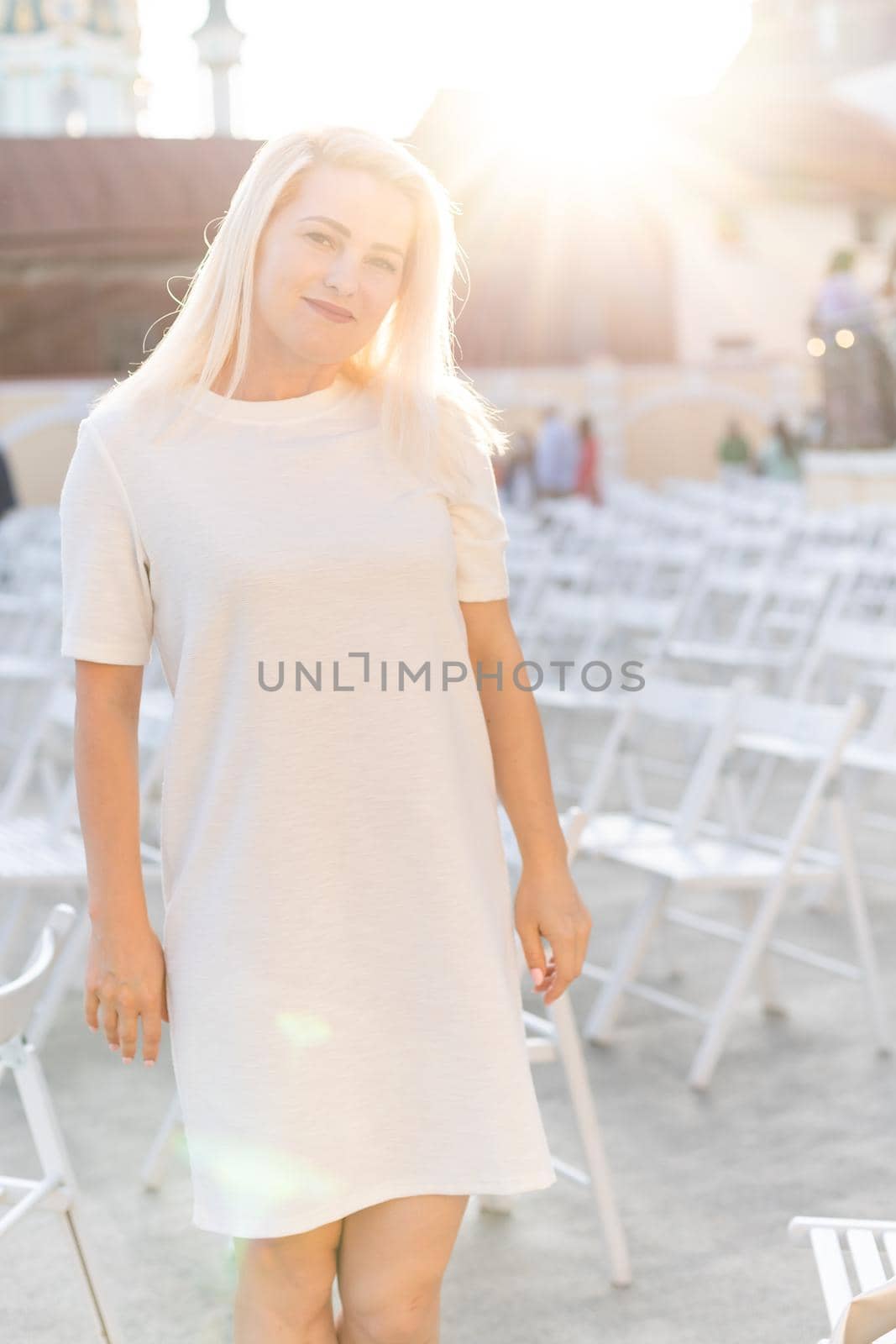 attractive woman dressed in white dress in summer open air theater on chair alone, spring street style fashion trend, social distancing