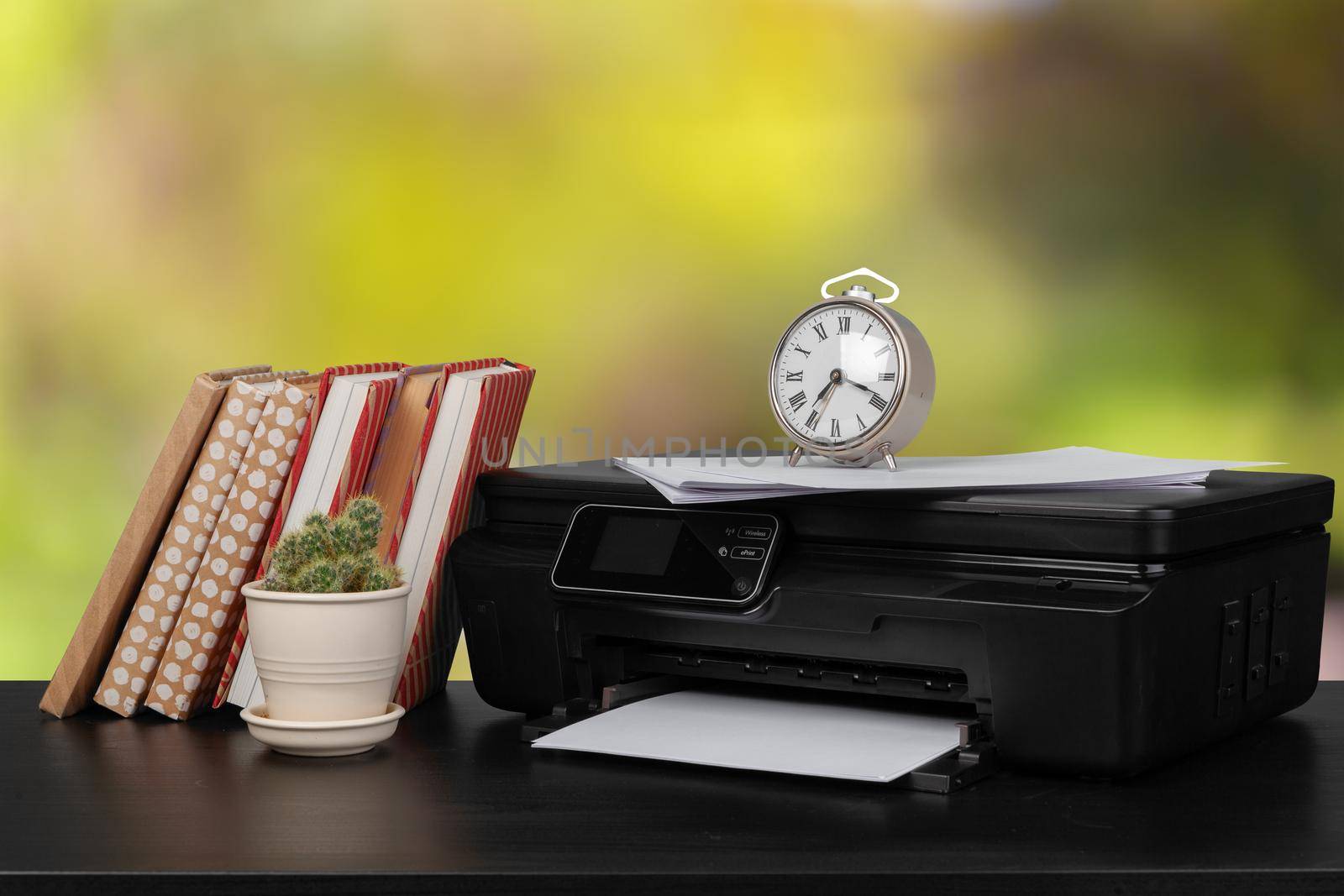 Stack of books and home printer against blurred background, close up