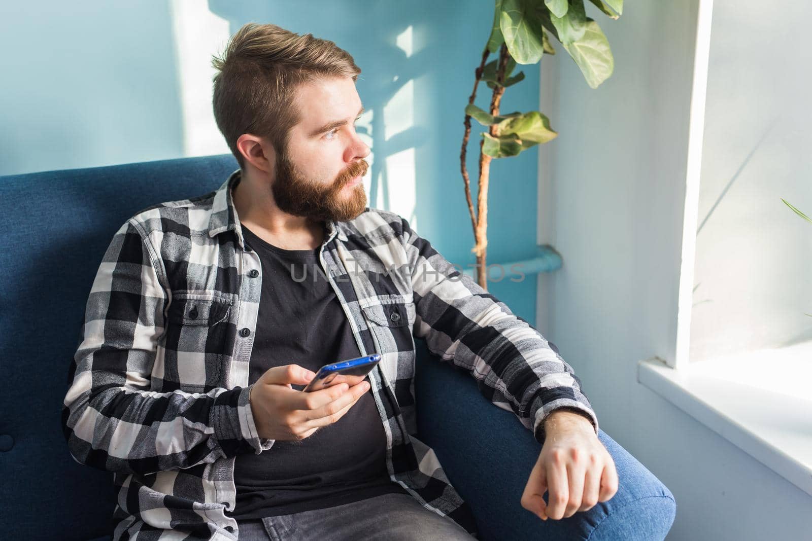 Technologies and leisure concept - Handsome man using smartphone sitting at home