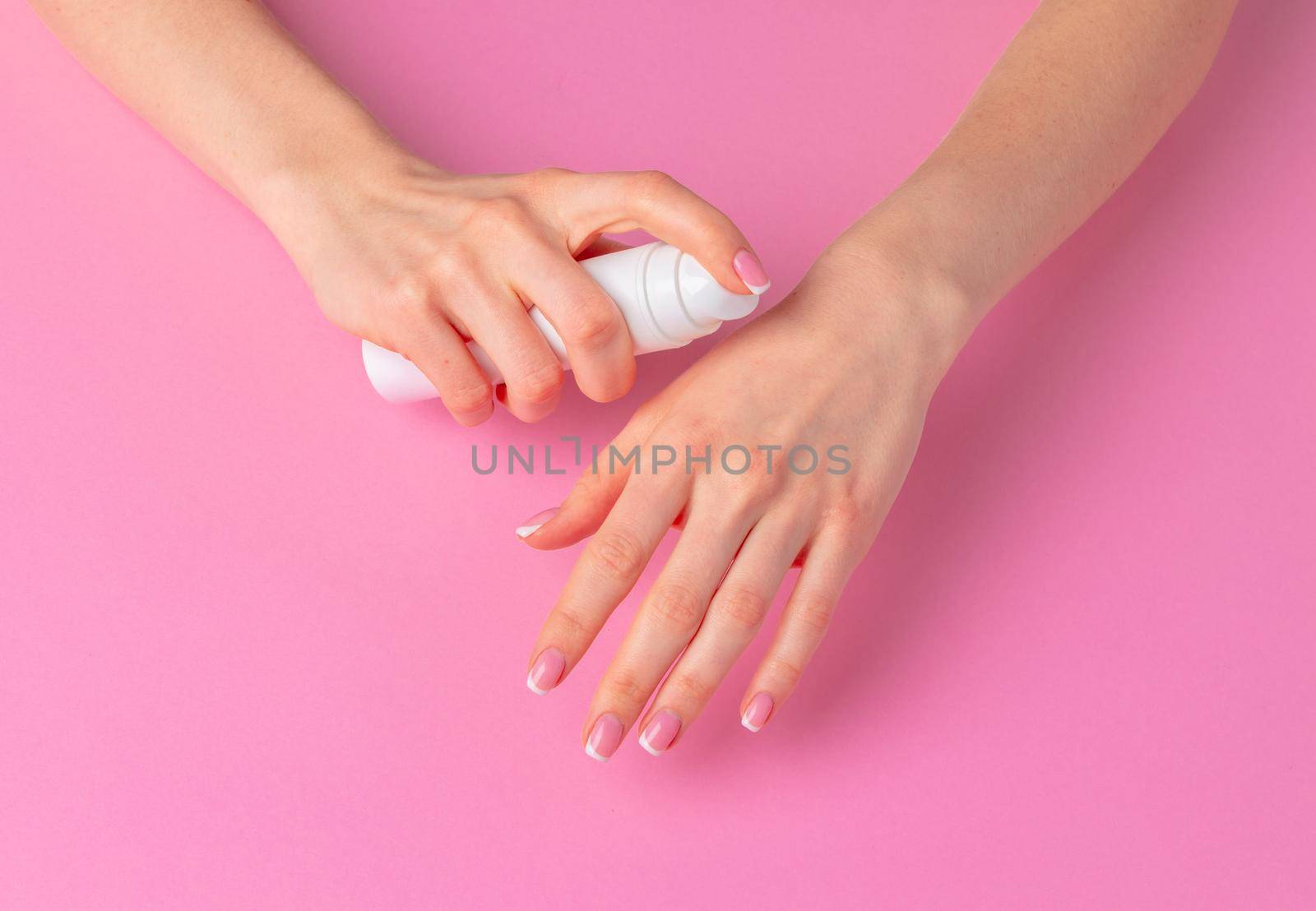 Female hand holding skincare product bottle on pink background