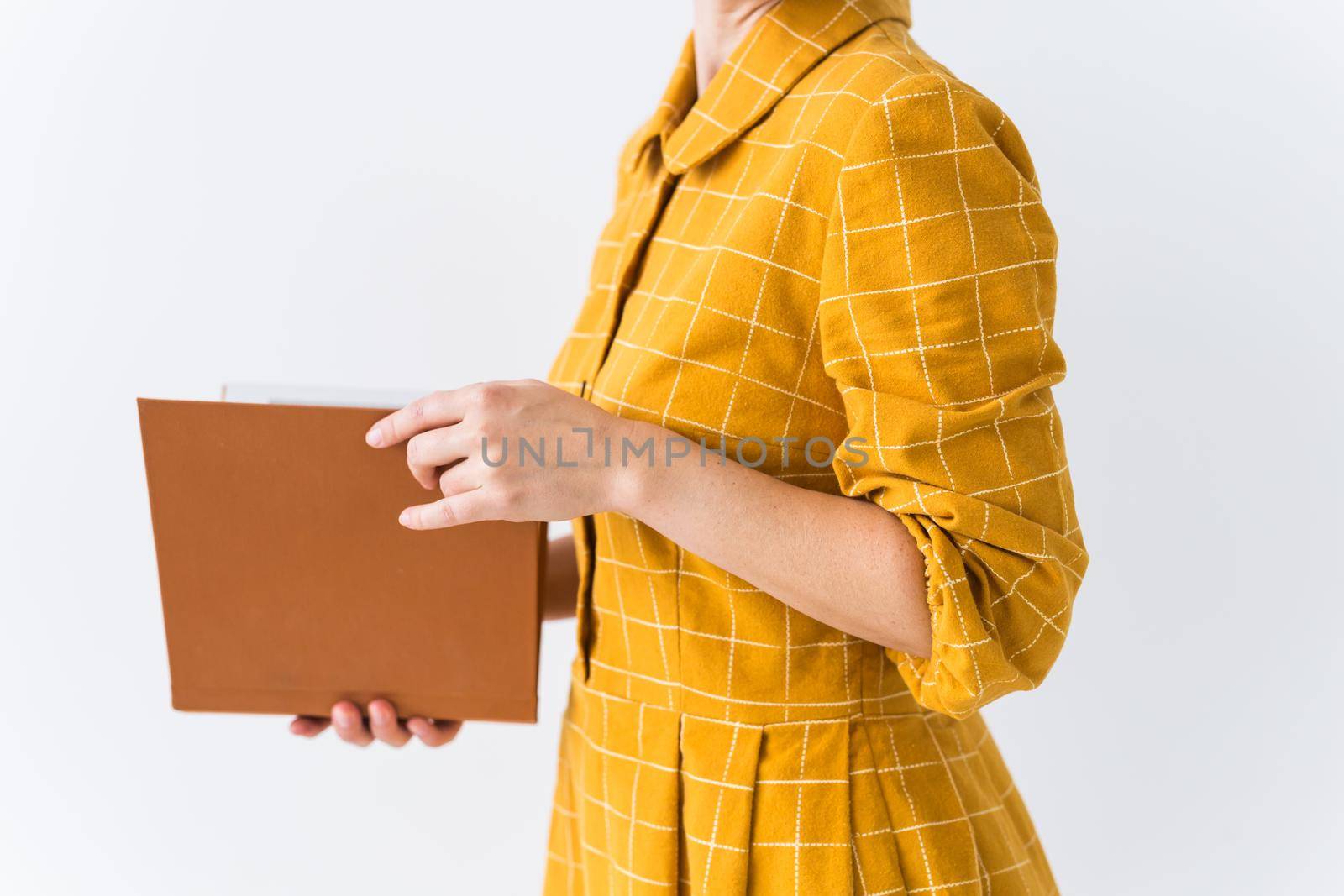 Portrait of a beautiful brunette girl in a yellow retro dress reading a book on white background.