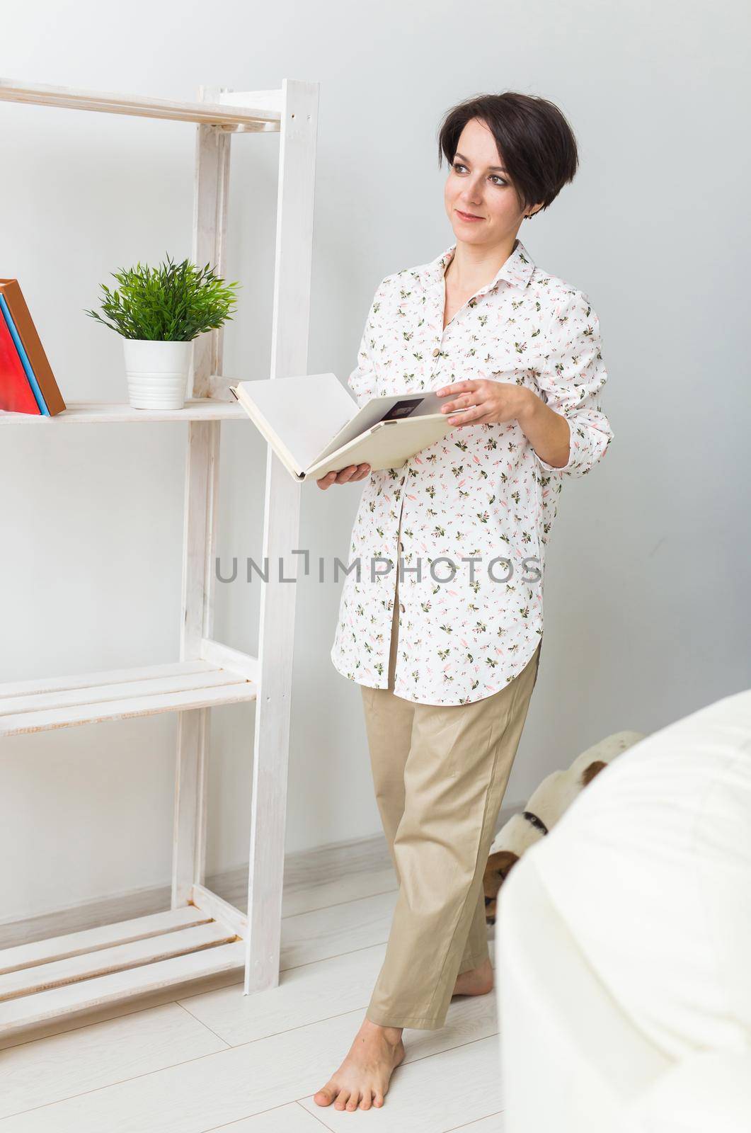 Beautiful young woman standing by the window reading a book