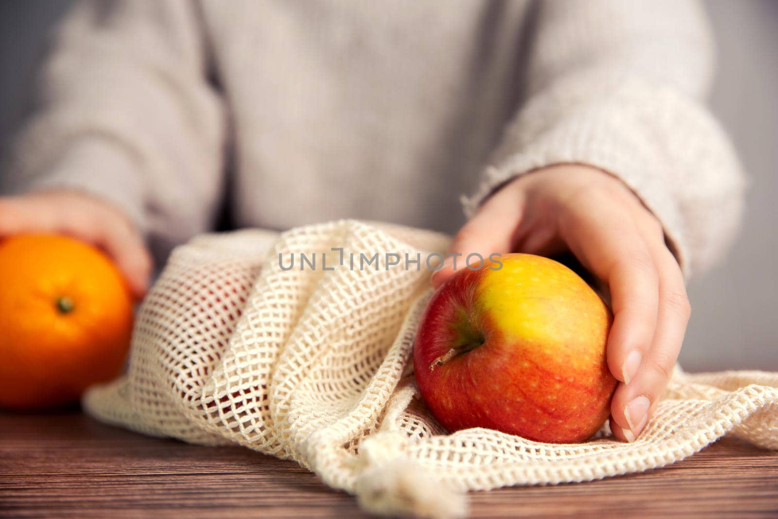Female hand with environmentally friendly net bag for shopping groceries with Fresh fruit, Apples and oranges, eco friendly net on wooden table by Annebel146