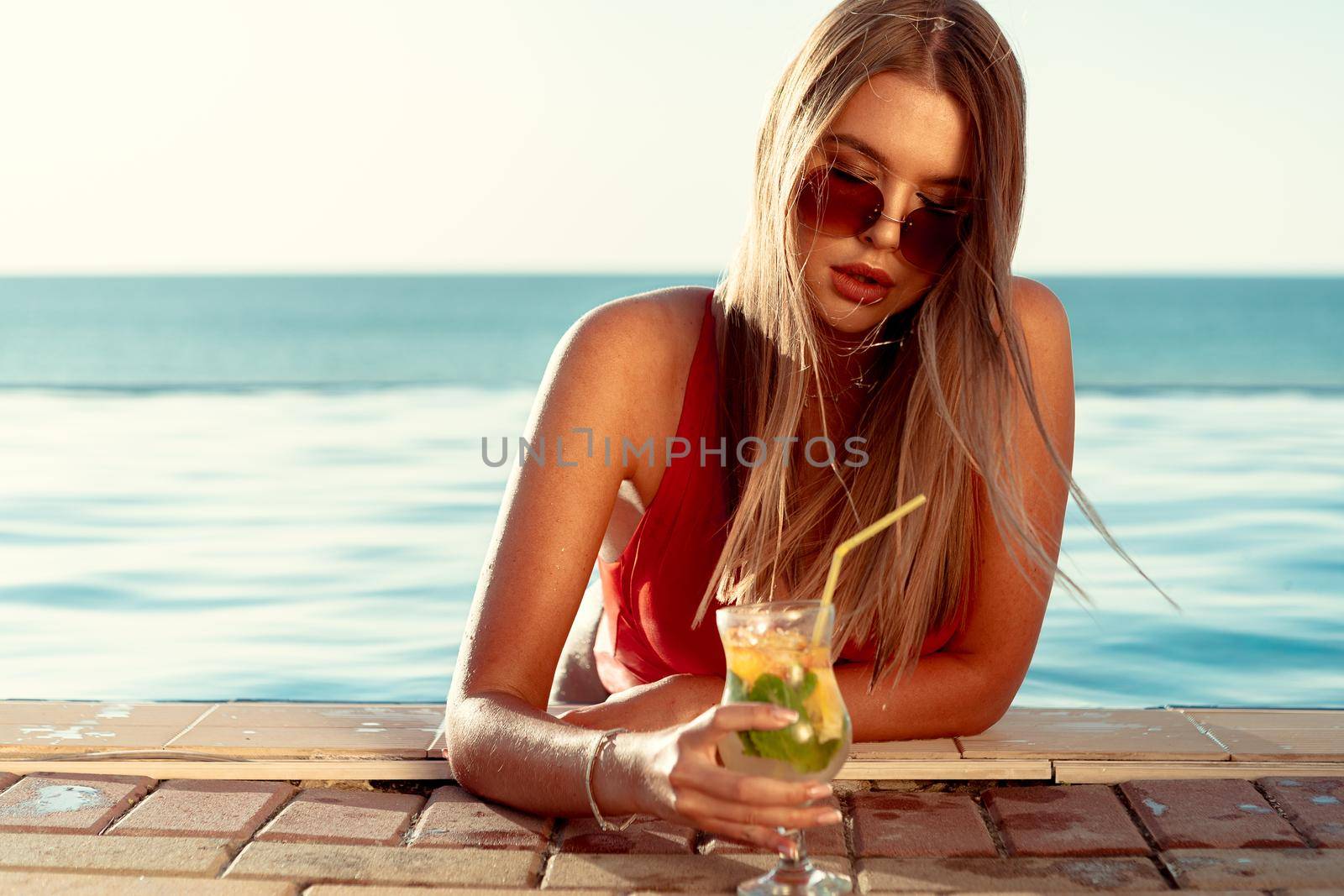 Tanned woman in red bikini in a pool with cocktail. High quality photo