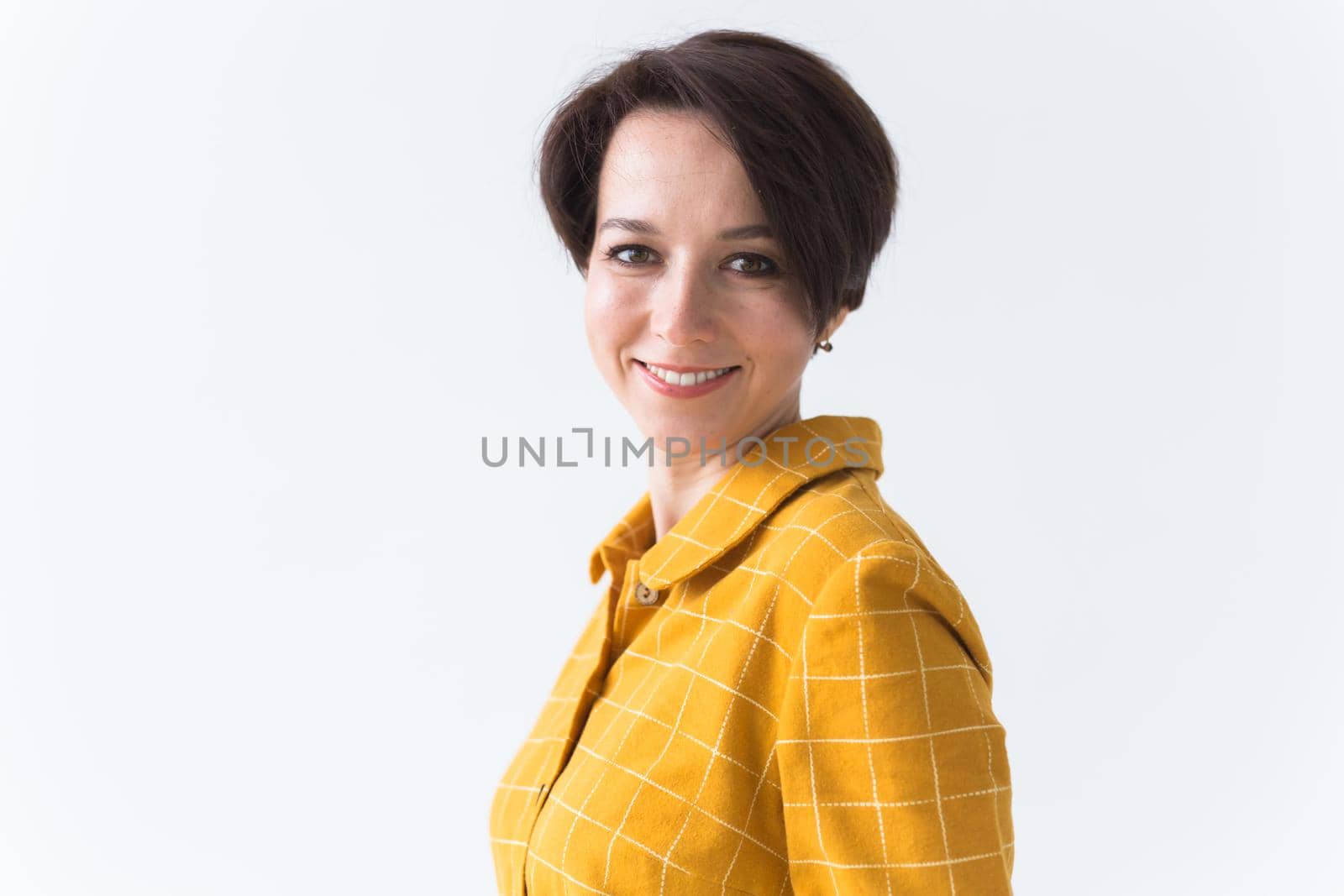 Portrait of a happy young woman in bright yellow dress over white room background. Beauty, fashion concept