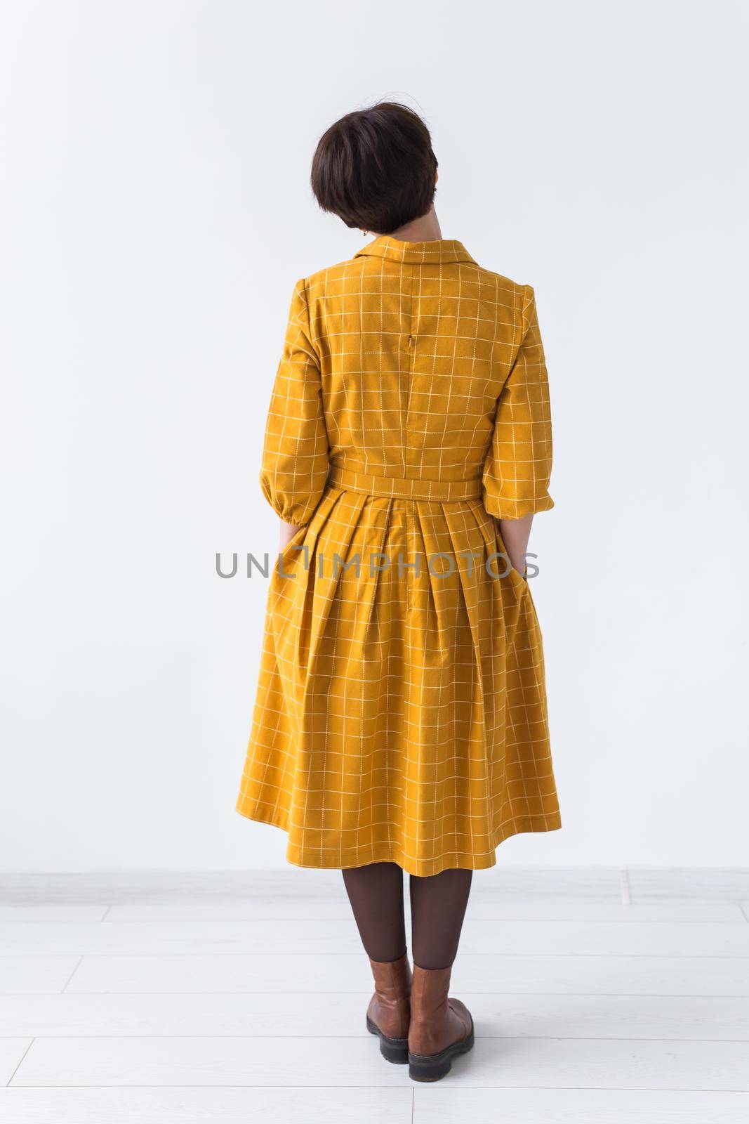 clothing, designer, people concept - back view of attractive woman in a yellow dress posing on white room. by Satura86