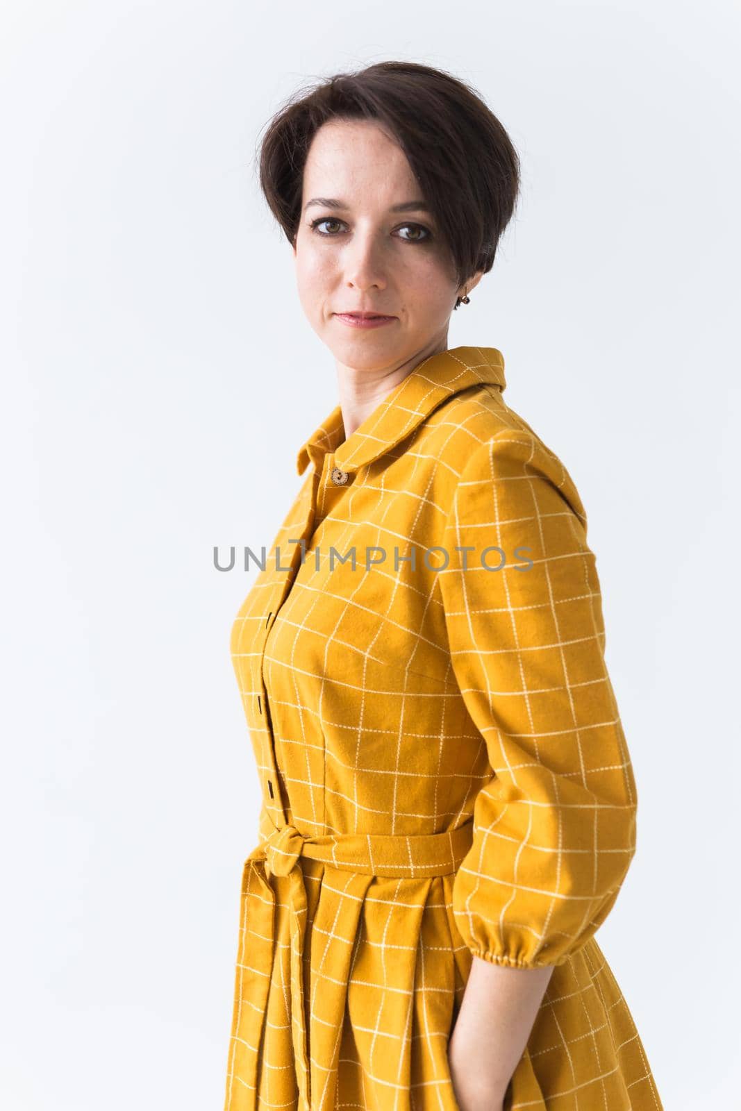 Portrait of a happy young woman in bright yellow dress over white room background. Beauty, fashion concept