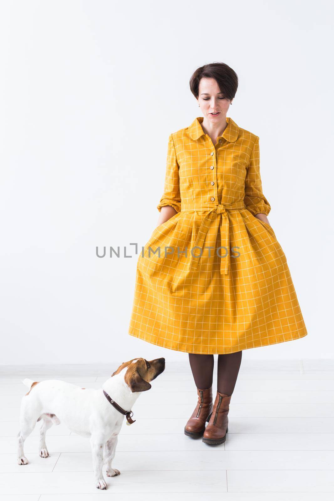 Cheerful young woman posing in a yellow dress with her beloved dog Jack Russell Terrier standing on a white background. The concept of casual wear and pets by Satura86